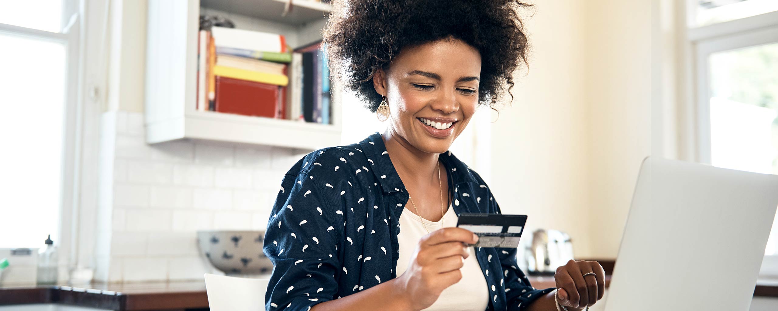 A woman sits at a computer and looks at her debit card, pleased she decided to open a checking account.