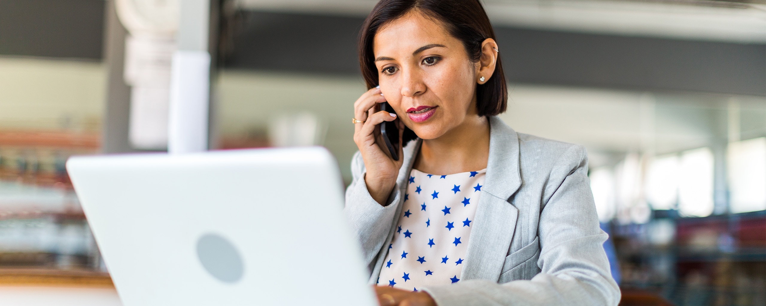 Business woman looking at laptop and holding mobile phone to ear