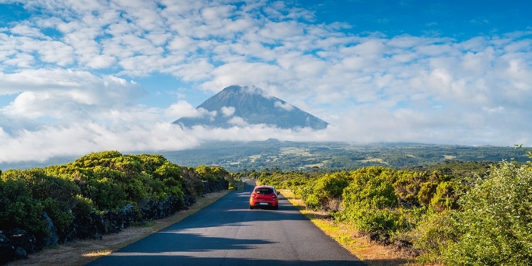 A red car drives down a quiet road toward a mountain