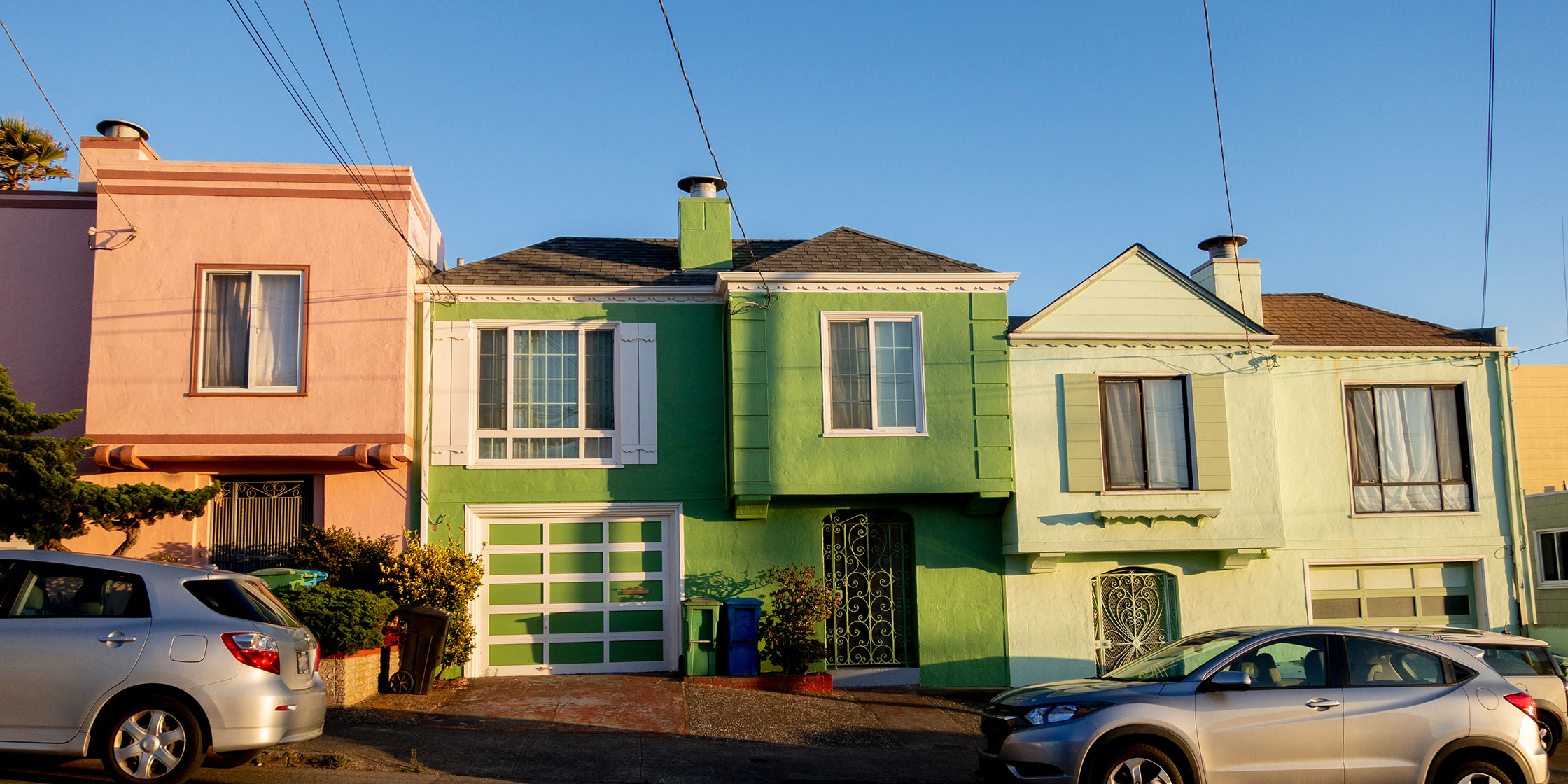 A street view of a row of three houses with two cars parked in front.